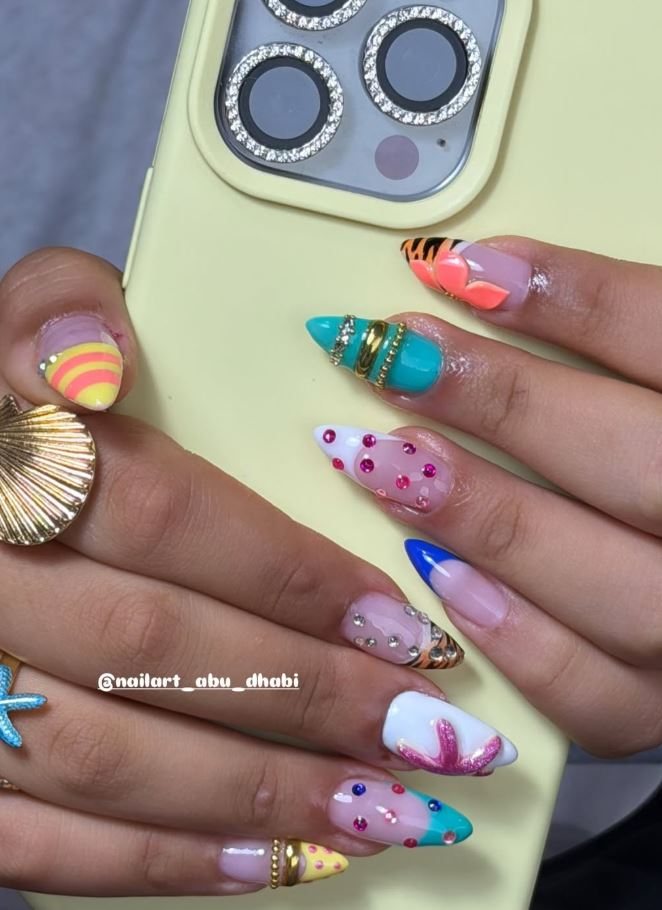 Bright multi-colour nail set with 3D detail, held beside a phone